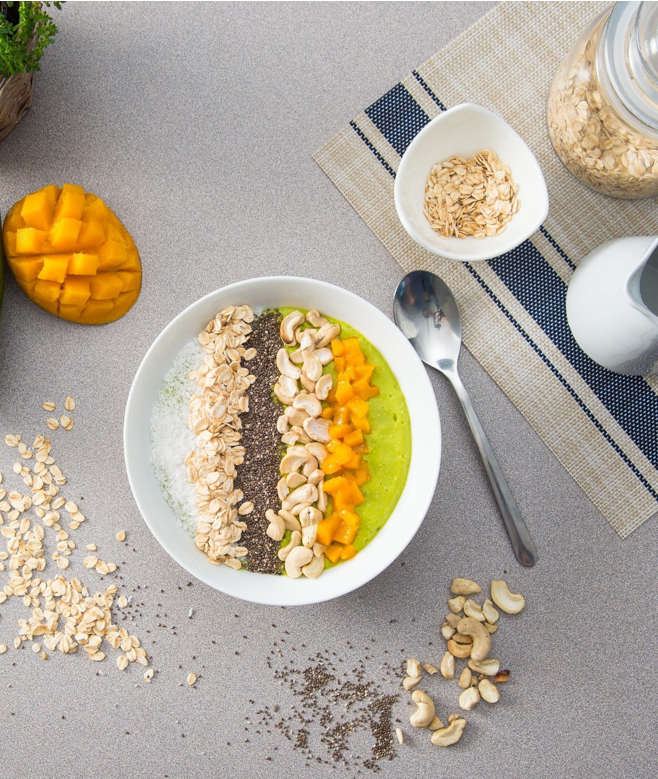bowl of super green healthy smoothie added with chopped mango, chia seeds and walnuts